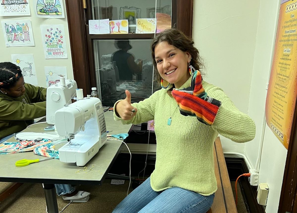 Smiling woman with a mitten on one hand giving a double thumbs-up